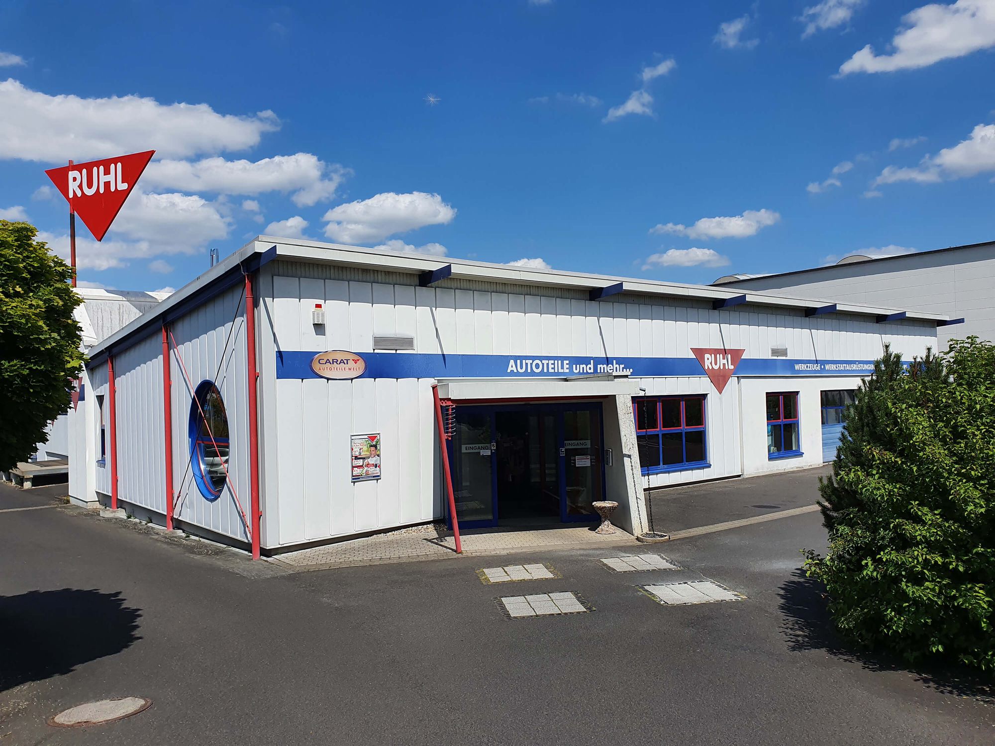 Firmengebäude von Ruhl & Co. GmbH mit weißer Fassade, blauen und roten Akzenten, großem Eingang und rotem Ruhl-Logo unter blauem Himmel mit weißen Wolken.